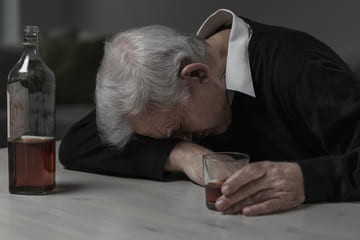 Дедушка лежит на столе с стаканом в руке